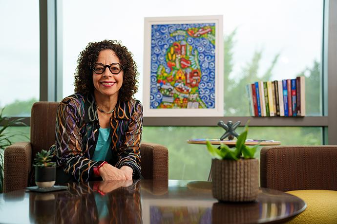 Dr. Florence Dallo in her office, with artwork of the state of Michigan and books in the background, and plants on the coffee table in front of her